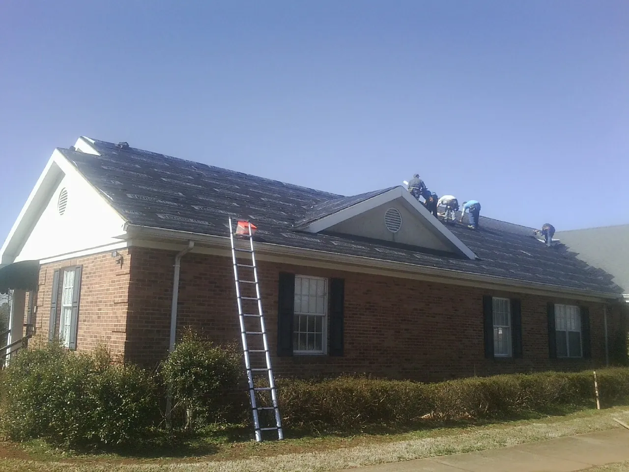 Crew tearing shingles off a brick ranch roof with a ladder set — Emergency Roof Repair work by our crew in Stanley